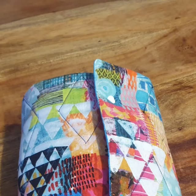Neceser enrollable de patchwork acolchado con estampados geométricos multicolores sobre una mesa de madera