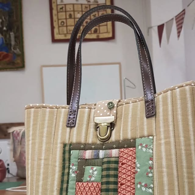 Bolso de patchwork con bloque Log Cabin en tonos tierra, verdes y granates, tela de rayas beige acolchada, asas de piel marrón y cierre metálico dorado